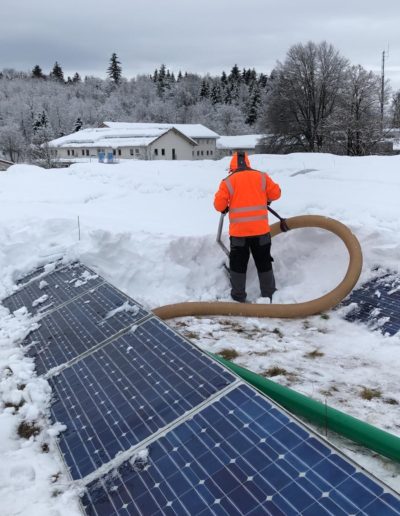 Arbeiter saugt Schnee von einem Flachdach